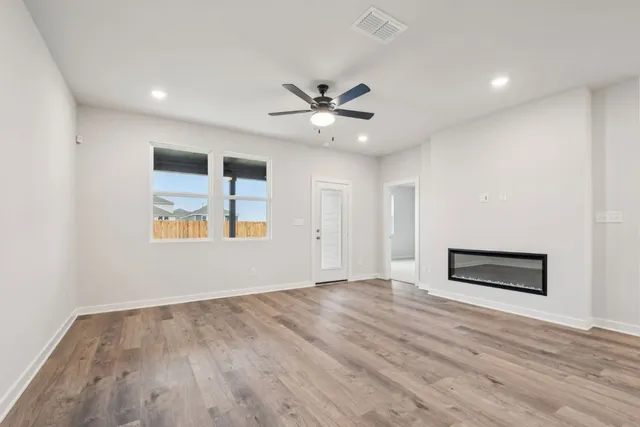 an empty room with wooden floor chandelier fan and windows