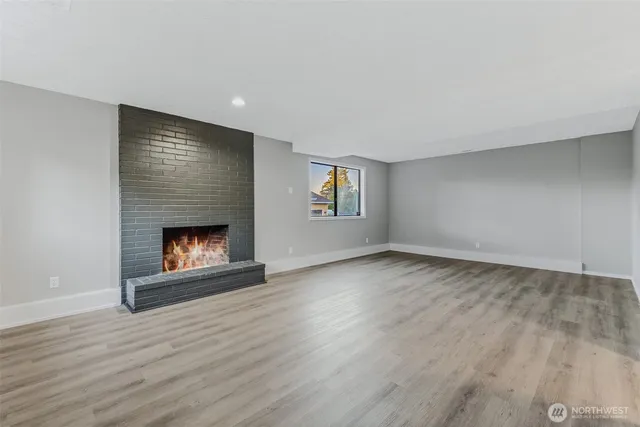 a view of an empty room with wooden floor fireplace and a window