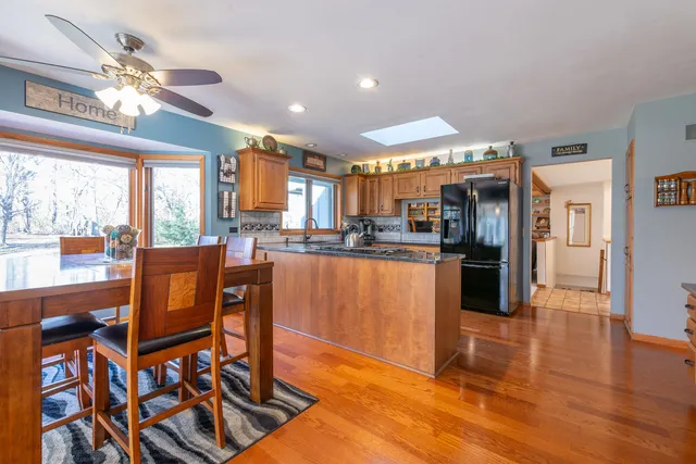 a kitchen with stainless steel appliances granite countertop a refrigerator a sink dishwasher a dining table and chairs with wooden floor