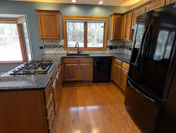 a kitchen with granite countertop a stove a sink dishwasher a refrigerator and wooden floor