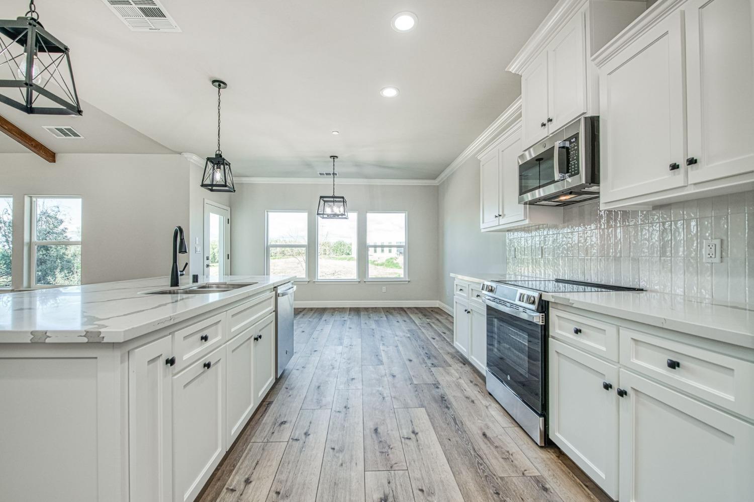 11271 Mountain View Drive Madera, CA 93636 - Photo 30 of 73 a kitchen with stainless steel appliances kitchen island granite countertop a stove a sink and white cabinets with wooden floor