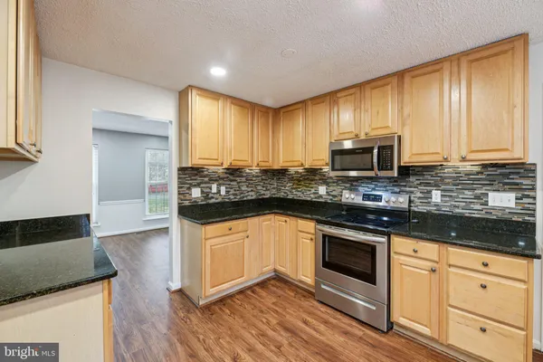 a kitchen with stainless steel appliances granite countertop wooden cabinets a sink a stove a dining table and chairs