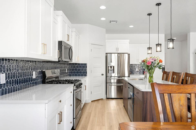 5963 Flattop Drive St. George, UT 84790 - Photo 13 of 45 Gourmet kitchen featuring white shaker cabinetry, quartz countertops, a dark blue geometric tile backsplash, stainless steel appliances, and a wood-finish island with pendant lighting