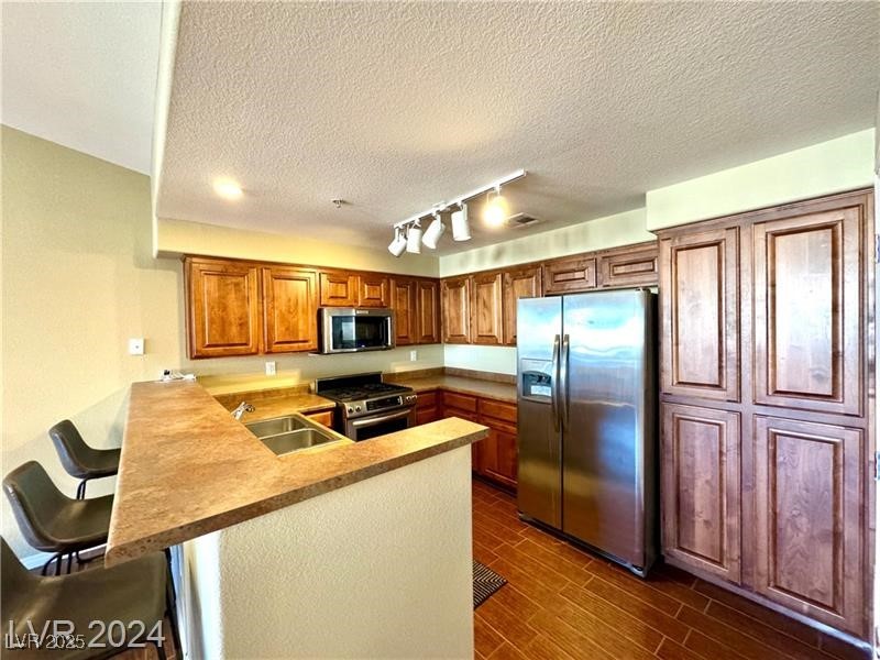 8777 West Maule Avenue, Unit 2103 Las Vegas, NV 89148 - Photo 2 of 33 Kitchen with appliances with stainless steel finishes, rail lighting, a peninsula, a kitchen breakfast bar, and brown cabinets