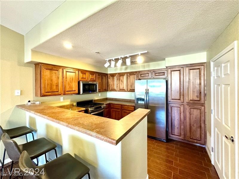 8777 West Maule Avenue, Unit 2103 Las Vegas, NV 89148 - Photo 7 of 33 Kitchen with a peninsula, appliances with stainless steel finishes, brown cabinets, a textured ceiling, and track lighting