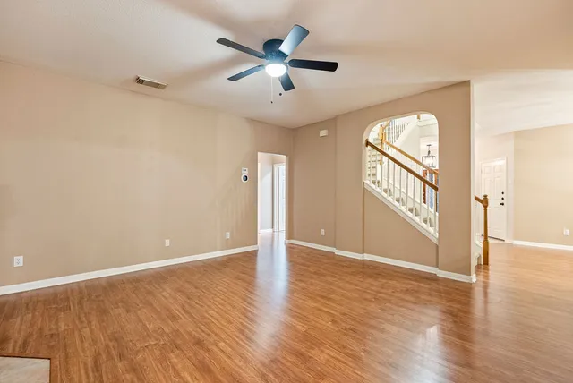 an empty room with wooden floor fan and windows