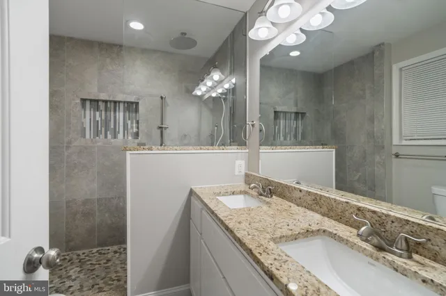 a bathroom with a granite countertop double vanity sink a mirror and shower