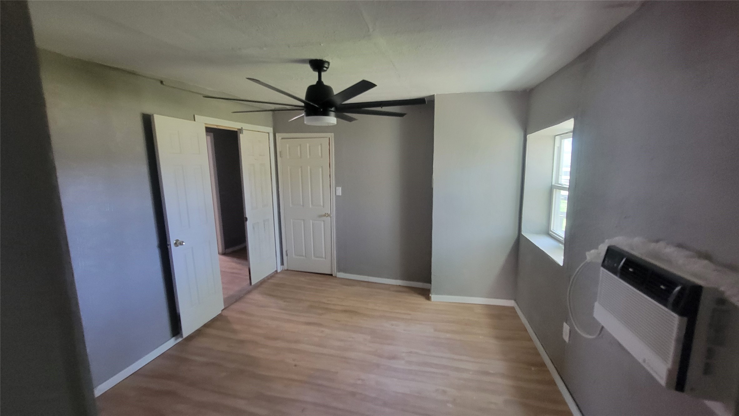 12018 Sandpiper Road Angleton, TX 77515 - Photo 30 of 48 This room features light wood flooring, neutral gray walls, a window with ample natural light, a ceiling fan, and wall-mounted air conditioning. It's a cozy space suitable for a variety of uses.