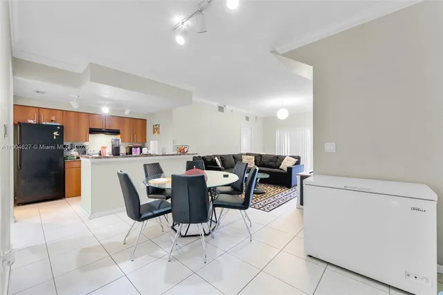 a living room with stainless steel appliances kitchen island granite countertop a table chairs and a refrigerator