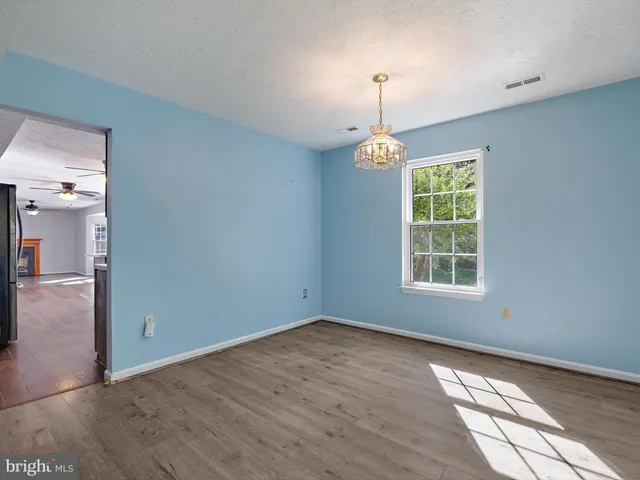 an empty room with wooden floor chandelier and windows