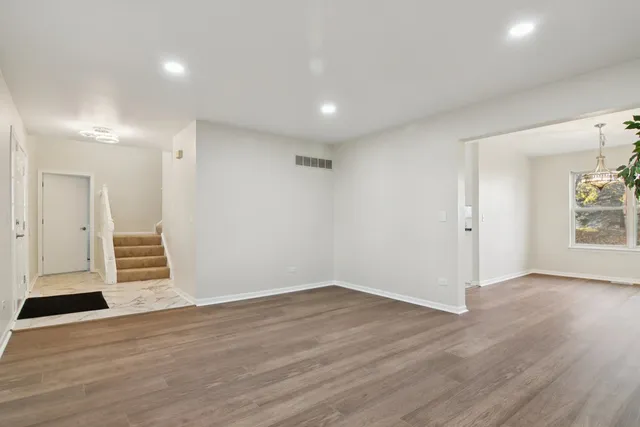 a view of an empty room with wooden floor and a kitchen