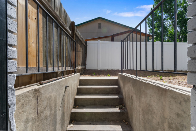 432 Calnette Drive Sandy, UT 84070 - Photo 40 of 48 Concrete staircase with black metal railings, flanked by a wood privacy fence and a white vinyl fence