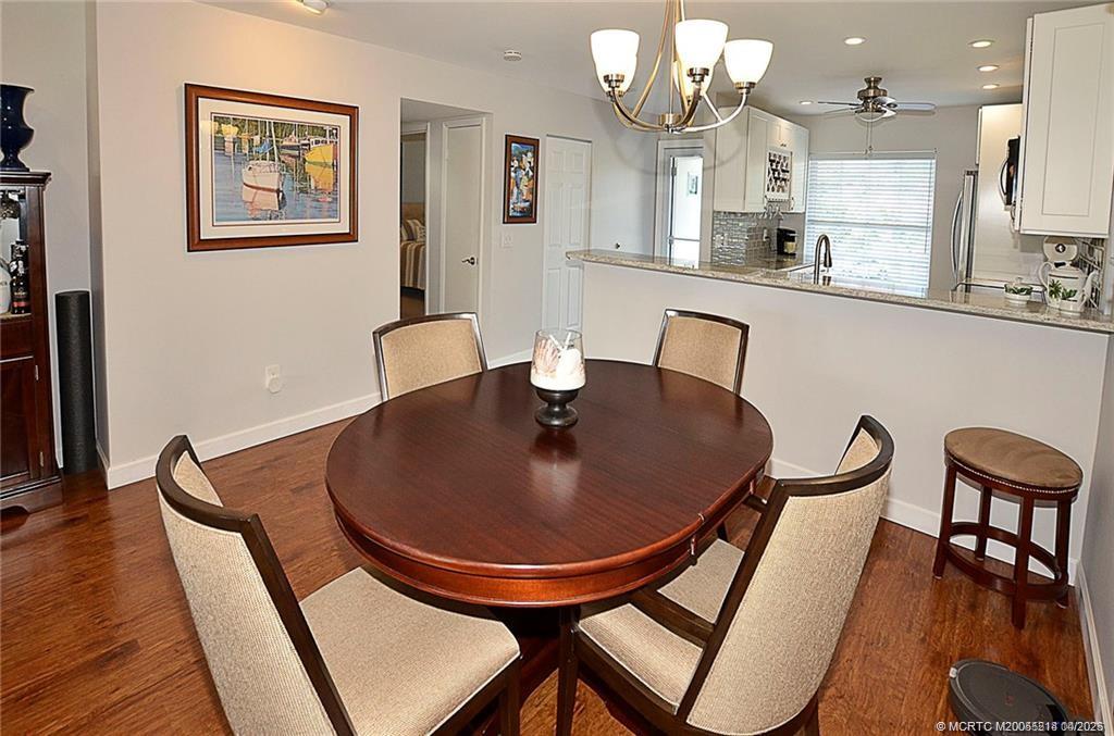 1854 Southwest Palm City Road, Unit 203 Stuart, FL 34994 - Photo 13 of 27 Spacious dining area with wood-look flooring opens to a beautifully updated kitchen featuring granite countertops, tile backsplash, bar seating, and recessed lighting.