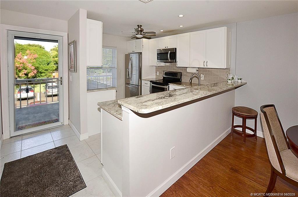 1854 Southwest Palm City Road, Unit 203 Stuart, FL 34994 - Photo 9 of 27 Updated kitchen featuring white shaker cabinetry, granite countertops, stainless steel appliances, tile backsplash, and a spacious breakfast bar perfect for additional seating
