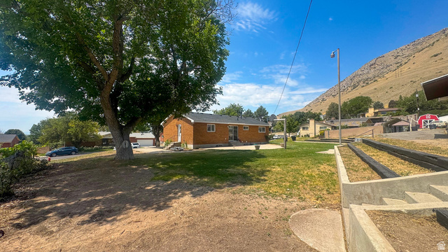 120 North 1230 E Street Springville, UT 84663 - Photo 37 of 60 Brick exterior ranch-style residence featuring a dark shingle roof, a rear concrete patio, and a mature shade tree