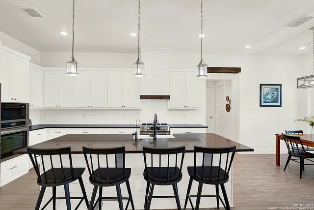 a kitchen with stainless steel appliances granite countertop a dining table chairs and white cabinets
