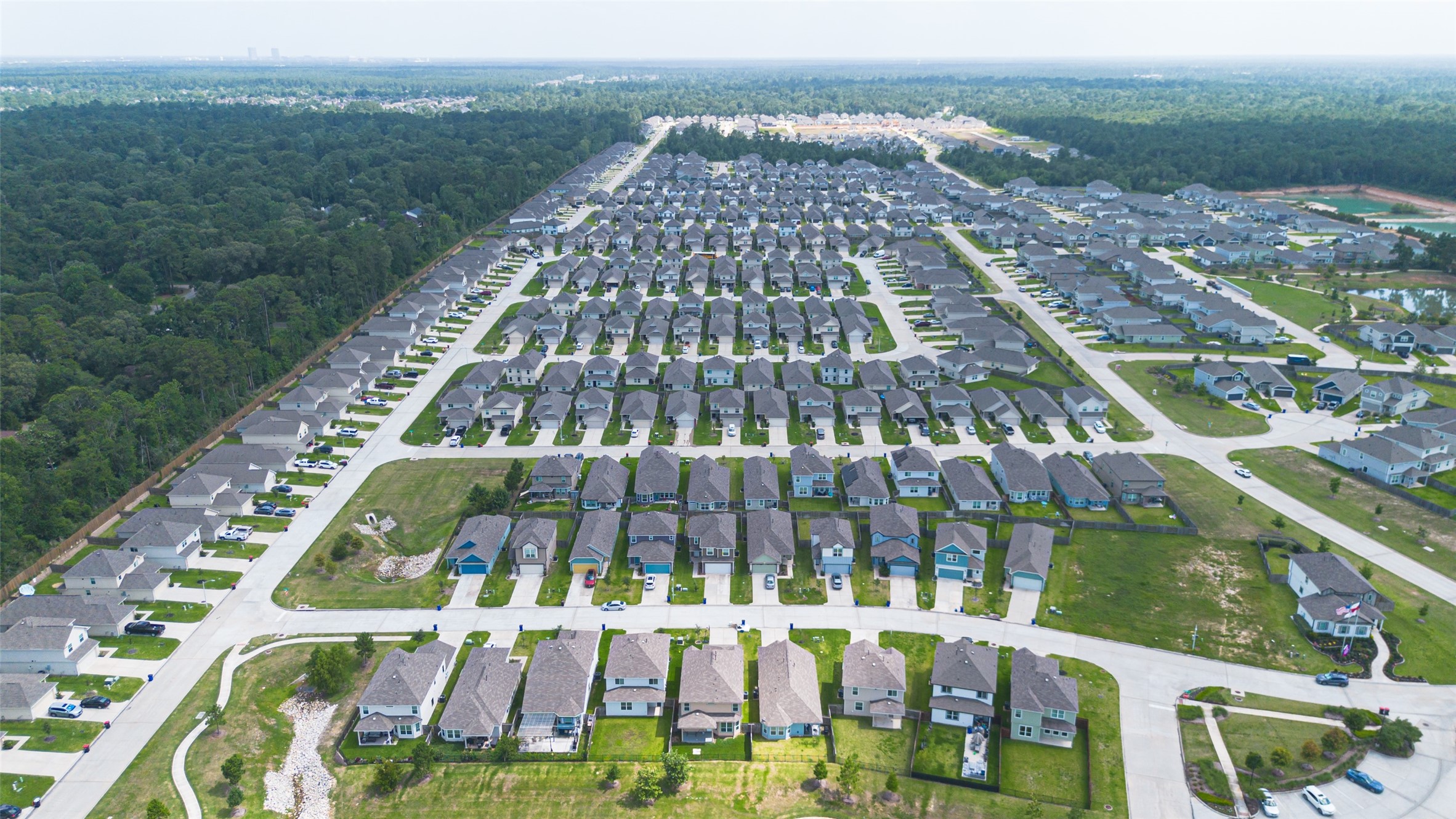2526 Sturgeon Way Conroe, TX 77384 - Photo 49 of 49 This aerial photo showcases a sprawling suburban neighborhood with rows of similar-style homes, neatly arranged along curved and straight roads, surrounded by green spaces and bordered by a wooded area.