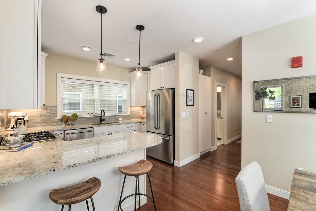 99 Brookley Road, Unit 1 Boston, MA 02130 - Photo 7 of 40 a kitchen with stainless steel appliances kitchen island granite countertop a refrigerator a stove a sink a dining table and chairs with wooden floor