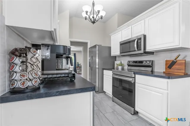 a kitchen with stainless steel appliances granite countertop a refrigerator a stove oven a sink dishwasher and white cabinets with wooden floor