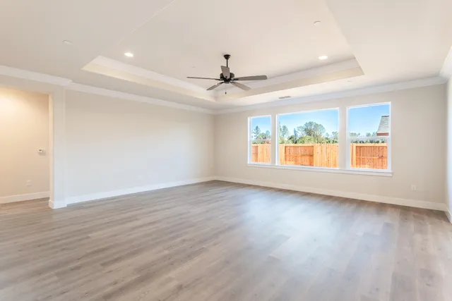 an empty room with wooden floor chandelier fan and windows