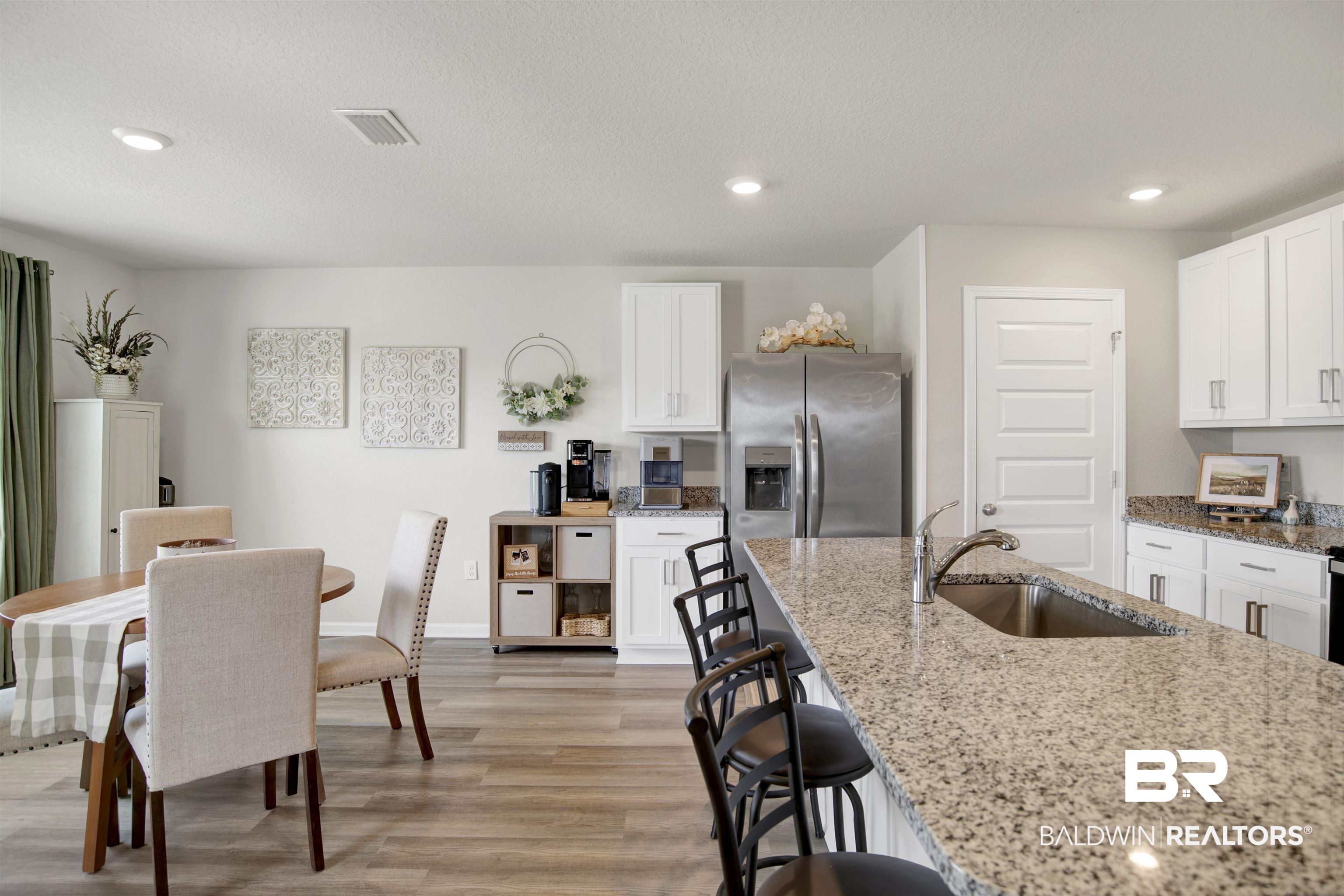 22301 Early Dawn Circle Foley, AL 36535 - Photo 25 of 45 Open-concept kitchen featuring granite countertops, stainless steel appliances, white cabinetry, a kitchen island with seating, and wood-finish flooring
