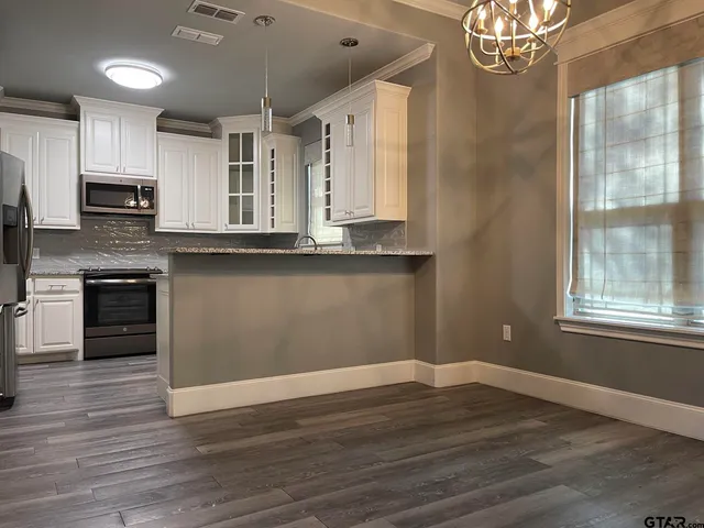 a kitchen with stainless steel appliances granite countertop a stove top oven a sink dishwasher a refrigerator and a dining table with wooden floor