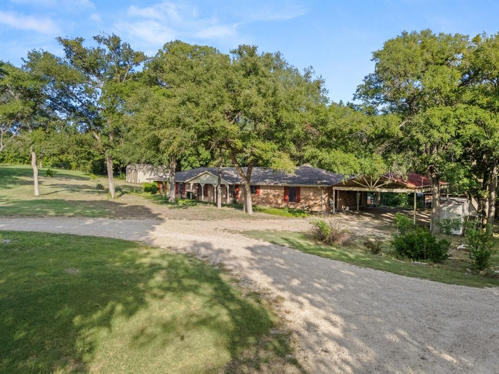 13539 Chapel Road Lorena, TX 76655 - Photo 34 of 37 Spacious property featuring a gravel driveway, mature trees, a brick exterior, an attached covered carport, and a detached shed