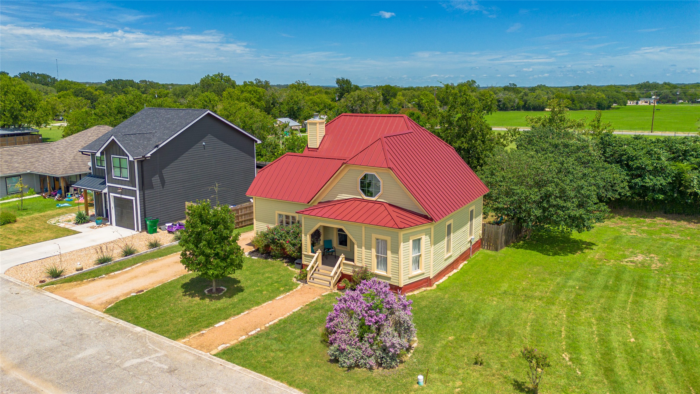 A vibrant red metal roof highlights this charming yellow cottage set on a green lawn.