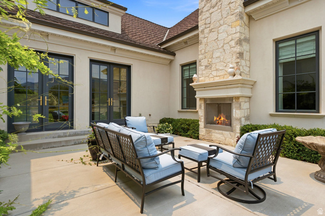 71 Farm Road Midway, UT 84049 - Photo 84 of 92 Expansive concrete patio featuring a stone-clad outdoor fireplace, multiple black-framed windows, and two sets of double French doors providing direct access to the interior