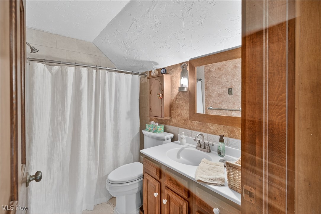 25700 Winona Road Homeworth, OH 44634 - Photo 22 of 49 Bathroom featuring vanity, lofted ceiling, curtained shower, a textured ceiling, and tile walls