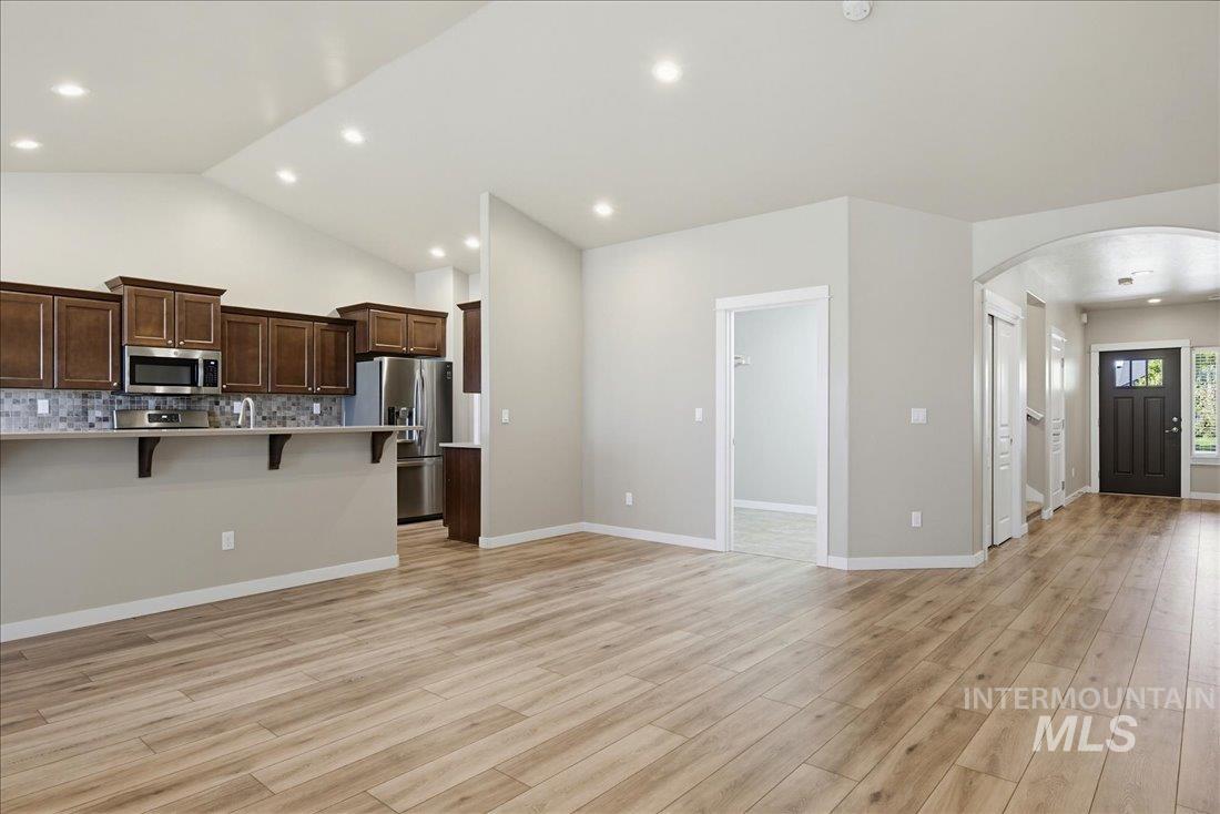 12460 West Azure Street Boise, ID 83713 - Photo 14 of 34 Open-concept living space featuring wood-finish flooring, vaulted ceilings, recessed lighting, and a kitchen with stainless steel appliances and a tile backsplash