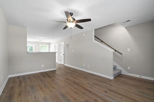 a view of an empty room with wooden floor and a ceiling fan