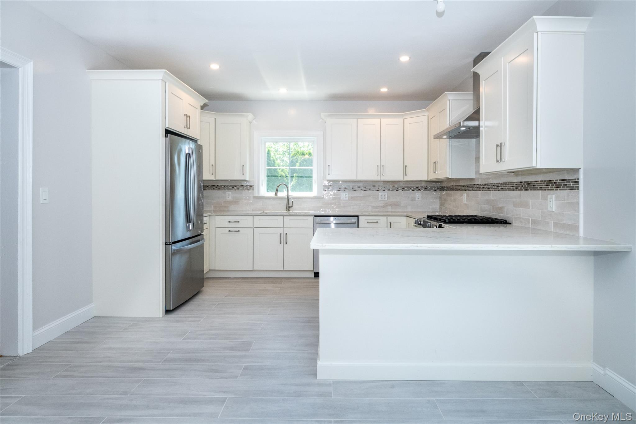7 Alpha Place, Unit FIRST New Rochelle, NY 10805 - Photo 7 of 25 Kitchen with stainless steel appliances, a peninsula, light countertops, decorative backsplash, and white cabinets