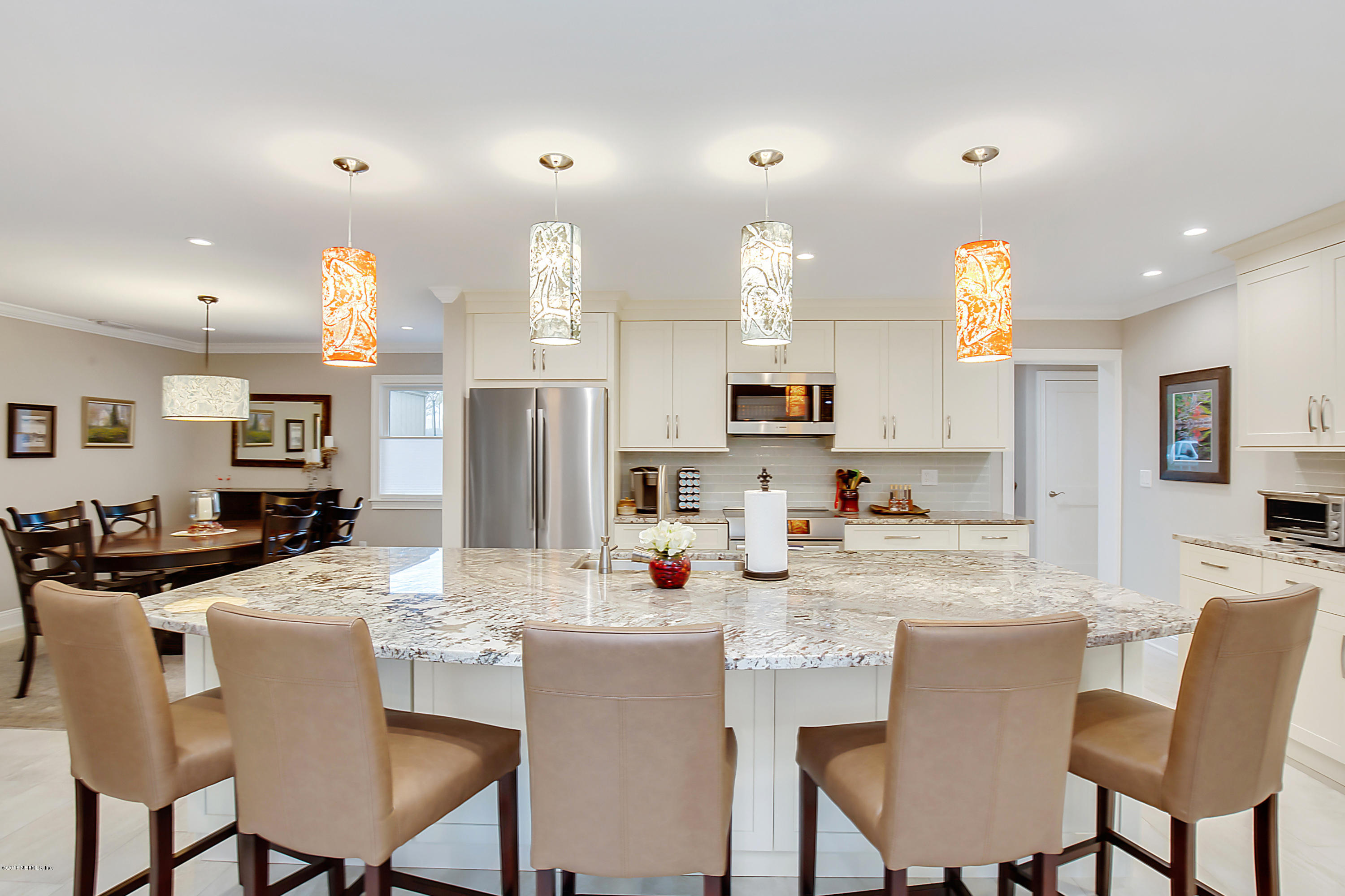a kitchen with kitchen island granite countertop a dining table chairs refrigerator and cabinets