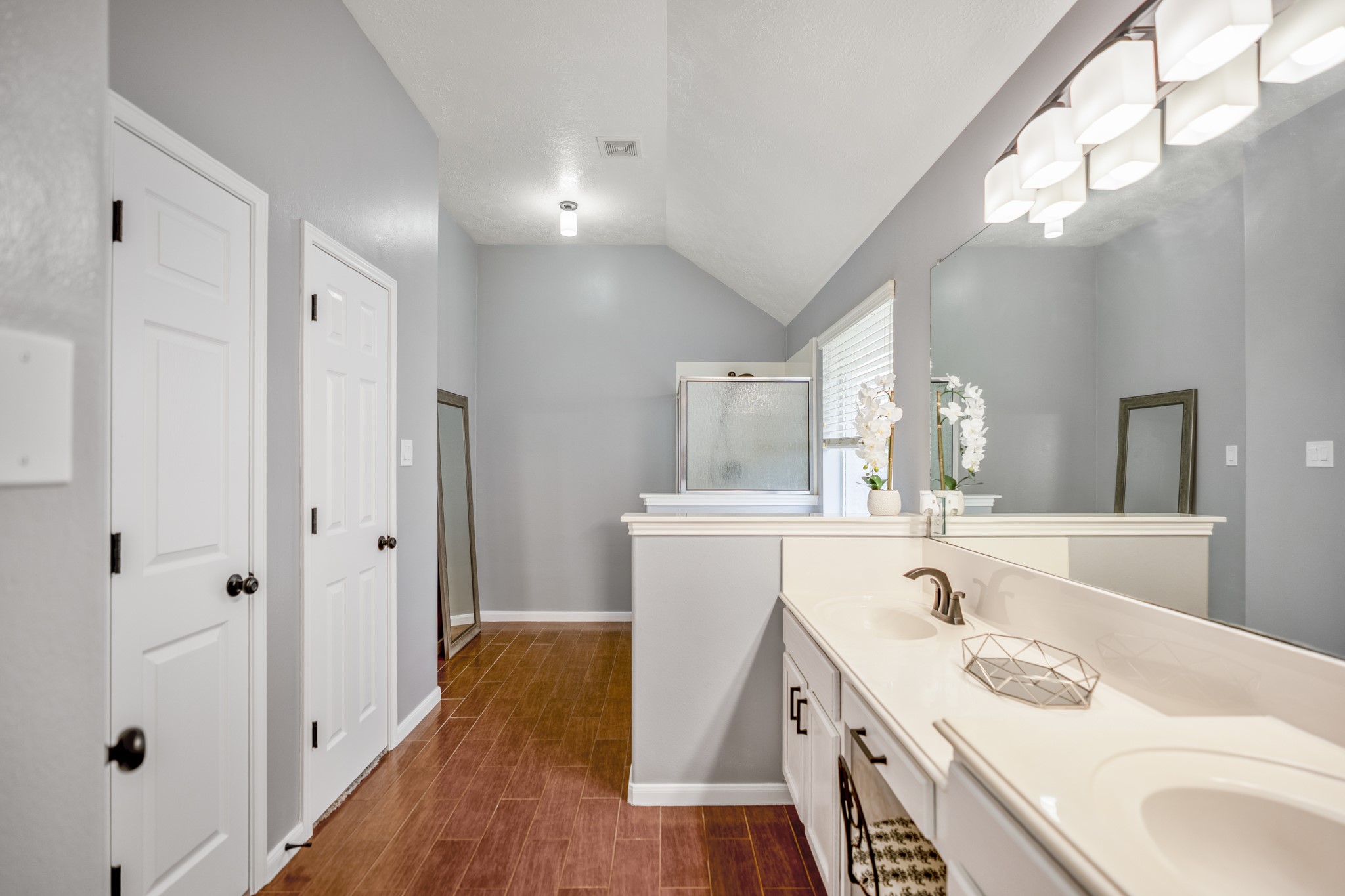 3411 Utah Beach Court Spring, TX 77388 - Photo 21 of 50 Down the length of the primary bath, the extended vanity offers a long run of counter space with two sinks, bright lighting, and mirrors along the right side. The doors along the left lead to the walk-in closet and private water closet, while the far end continues toward the soaking tub and shower area, keeping the suite functional from bedroom to bath to storage.