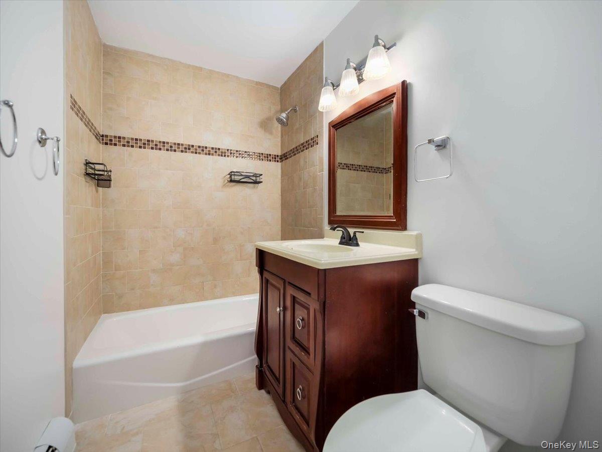27 Tanager Road, Unit 2702 Monroe, NY 10950 - Photo 25 of 35 Bathroom featuring a tiled shower surround with decorative accent band, a white bathtub, and a wood-finish vanity with an integrated sink