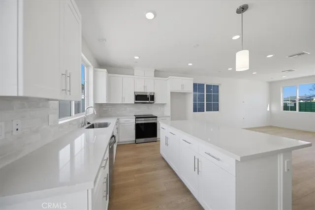 a large white kitchen with a stove top oven a sink a kitchen island and stainless steel appliances