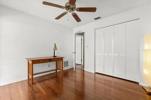 a view of an empty room with window a ceiling fan and wooden floor