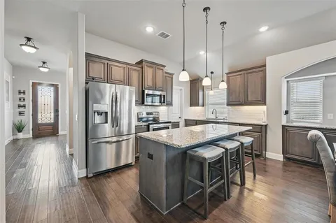 a kitchen with stainless steel appliances granite countertop a refrigerator a sink dishwasher a stove and white countertops with wooden floor