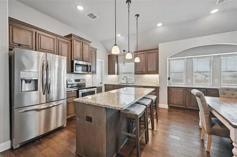 a kitchen with granite countertop a refrigerator a stove a sink dishwasher a dining table and chairs with wooden floor