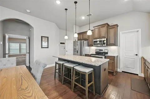 a kitchen with stainless steel appliances kitchen island granite countertop a table chairs in it and wooden floors
