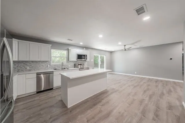 a large white kitchen with kitchen island a sink stainless steel appliances and cabinets
