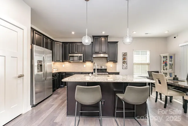 a kitchen with stainless steel appliances granite countertop a table chairs refrigerator and microwave