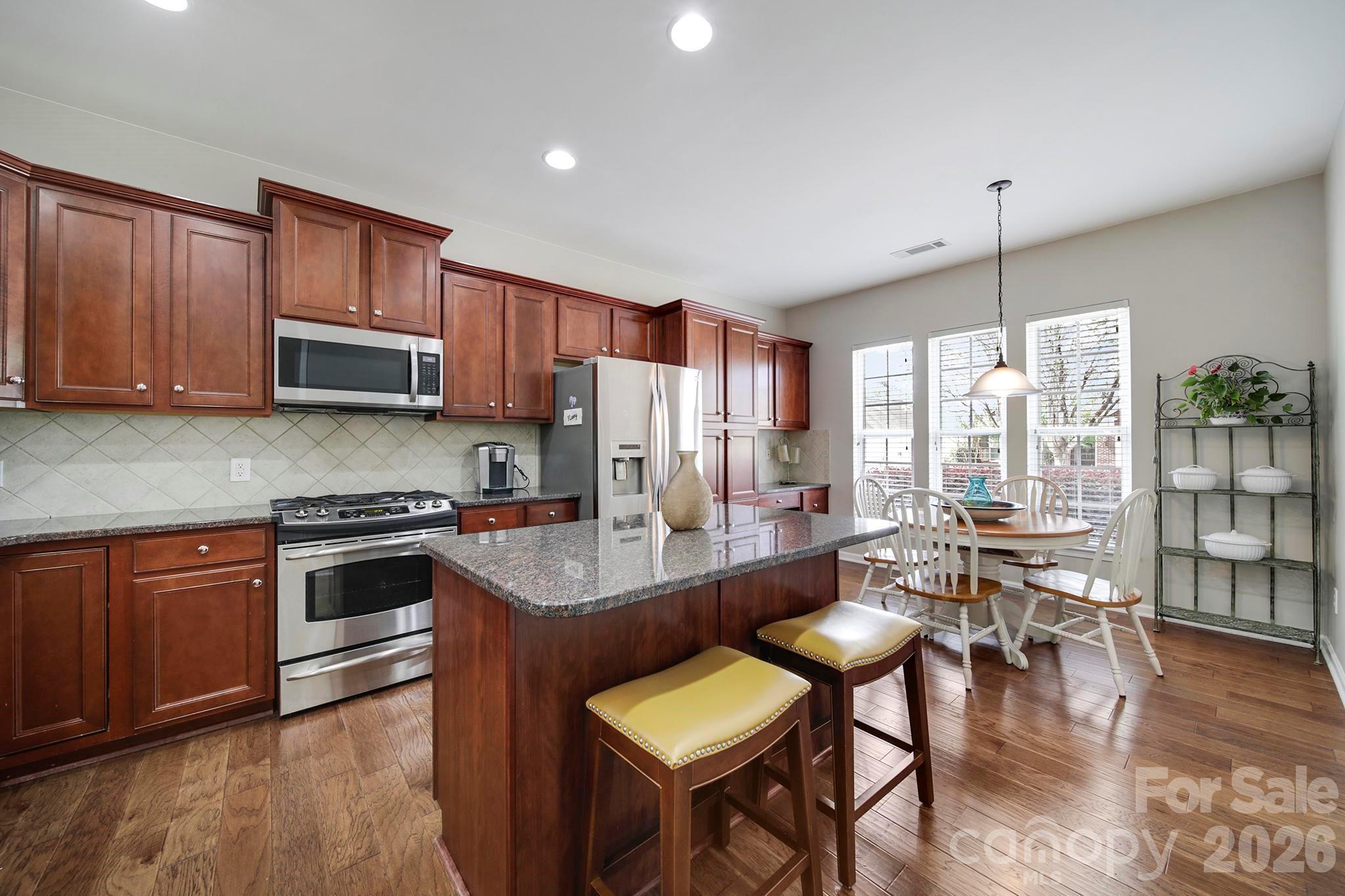 55414 Derringer Avenue Fort Mill, SC 29707 - Photo 4 of 45 a kitchen with stainless steel appliances granite countertop a stove top oven a refrigerator a dining table and chairs with wooden floor