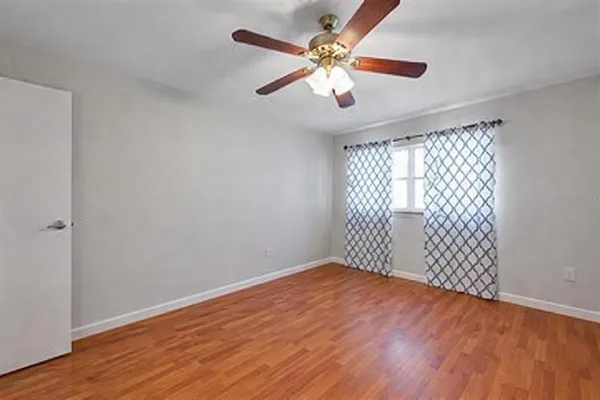an empty room with wooden floor fan and windows