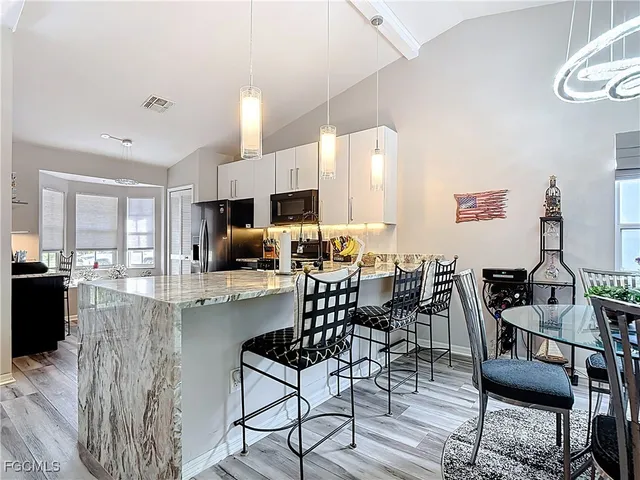a kitchen with stainless steel appliances kitchen island granite countertop a dining table chairs and a refrigerator