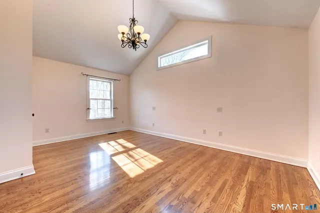 an empty room with wooden floor chandelier and windows