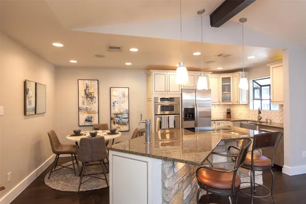 a kitchen with stainless steel appliances kitchen island granite countertop a dining table chairs and granite counter tops