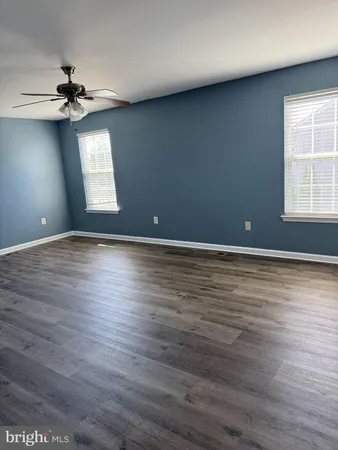 an empty room with wooden floor chandelier fan and windows