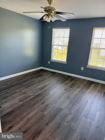 an empty room with wooden floor chandelier fan and windows